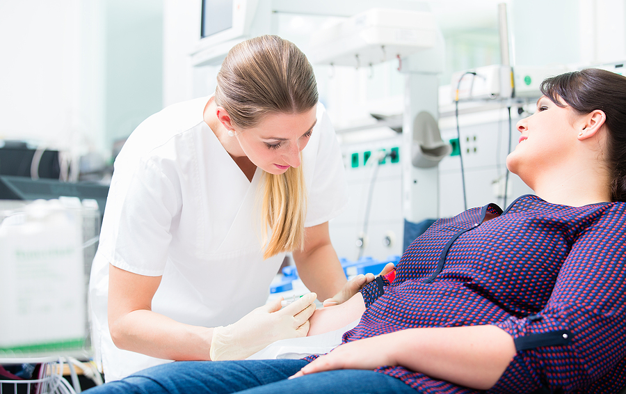 Phlebotomist drawing blood from a female patient in a clinic.